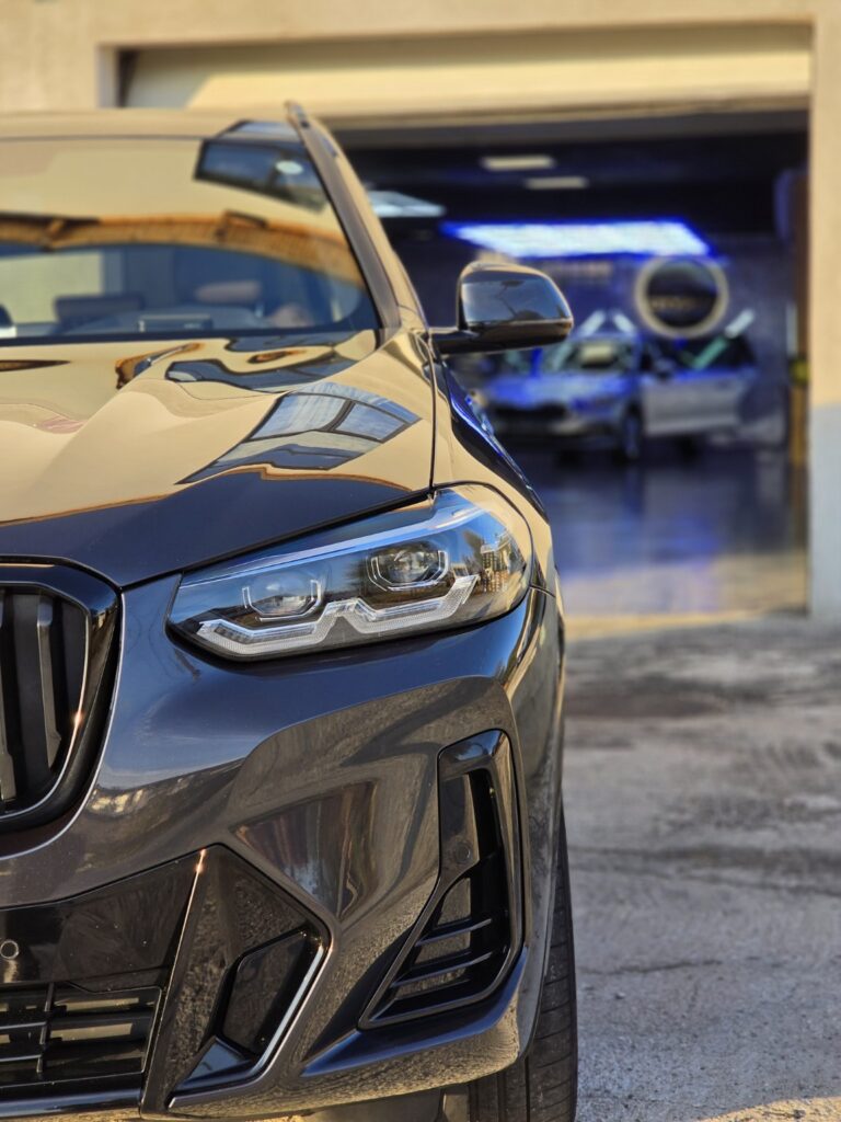 Detaliu cu farul și reflexiile caroseriei unui BMW în fața atelierului City Detailing